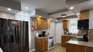 A modern kitchen with a stainless steel refrigerator, wooden cabinets, granite countertops, and a tiled backsplash.
