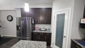 Una cocina compacta con armarios oscuros, un refrigerador de acero inoxidable, una encimera de granito y una pequeña isla.