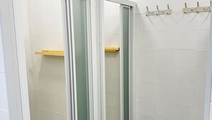 A bathroom with white tiled walls, a glass shower enclosure, and a wooden shelf. - Single capsule in room of 16 capsules (El Palmar de Vejer)