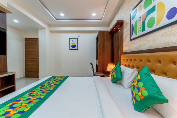 Habitación de hotel con una cama grande, cabecera de madera, una obra de arte colgada en la pared, un armario de madera y una mesita de noche con una lámpara.