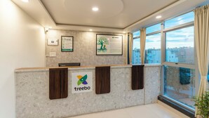 A reception desk with a 'treebo' logo, framed informational posters, and a large window with a view of buildings. - Treebo Silent Woods (Bengaluru)