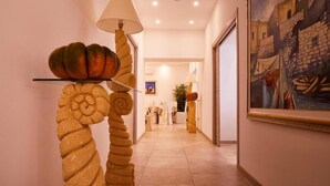 A hallway with a spiral floor lamp, a painting on the wall, and a glimpse of a room with a plant and a table. - Hotel Alba D'Amore (Lampedusa)