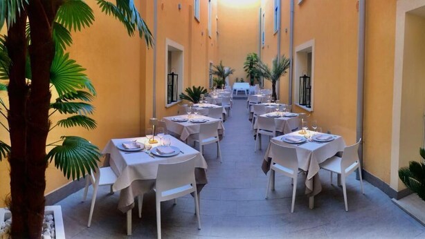 A corridor with tables set for dining, palm trees, and a yellow wall. - Hotel Alba D'Amore (Lampedusa)