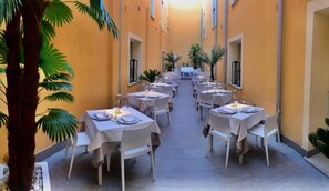Un couloir avec des tables dressées pour le repas, des palmiers et un mur jaune.