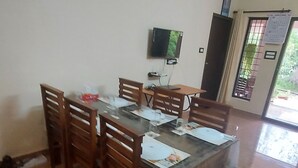 Un coin repas avec une table et des chaises en bois, une horloge au mur et un téléviseur fixé au-dessus de la table.
