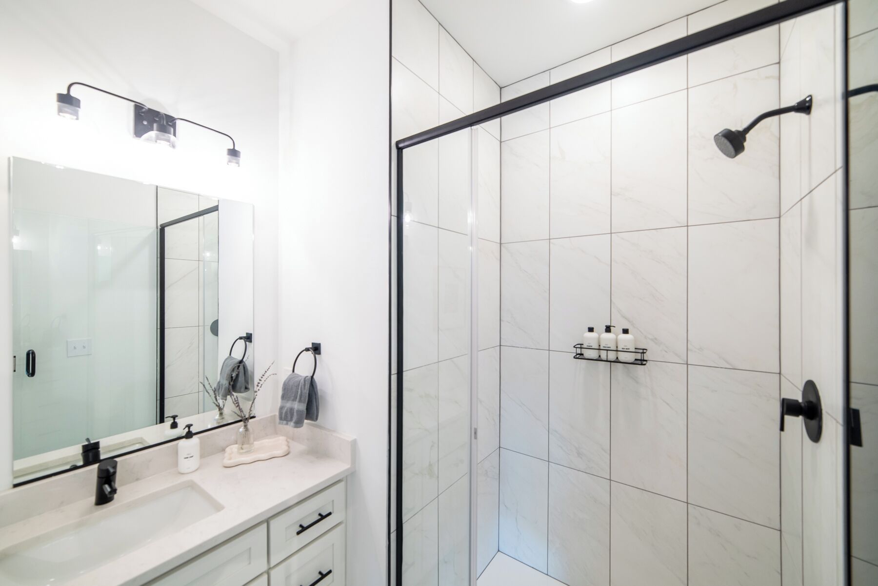 Un baño moderno con cabina de ducha de vidrio, un espejo grande y un tocador blanco con lavabo y toallero.