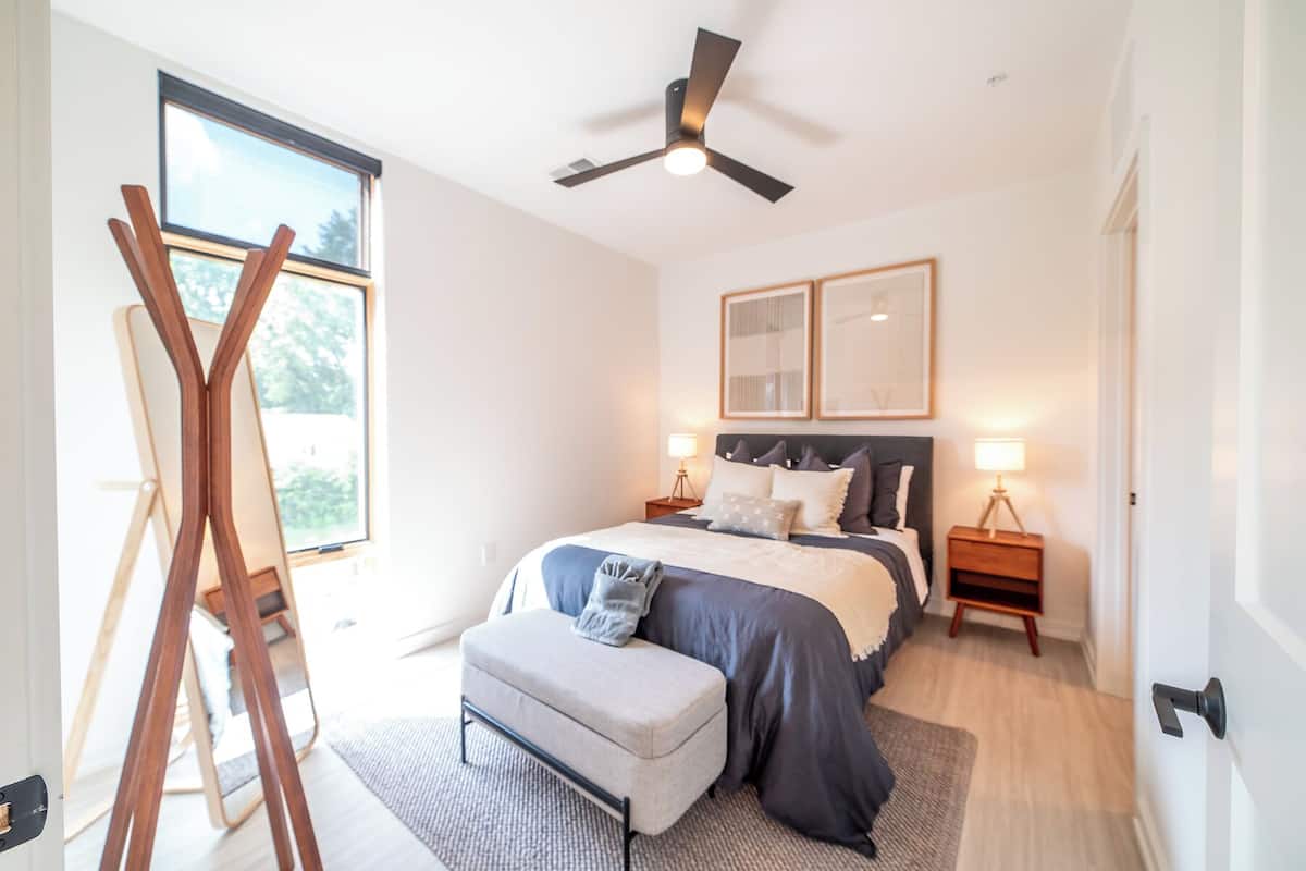 A modern bedroom with a large bed, bedside tables, a ceiling fan, and a view of the outdoors.