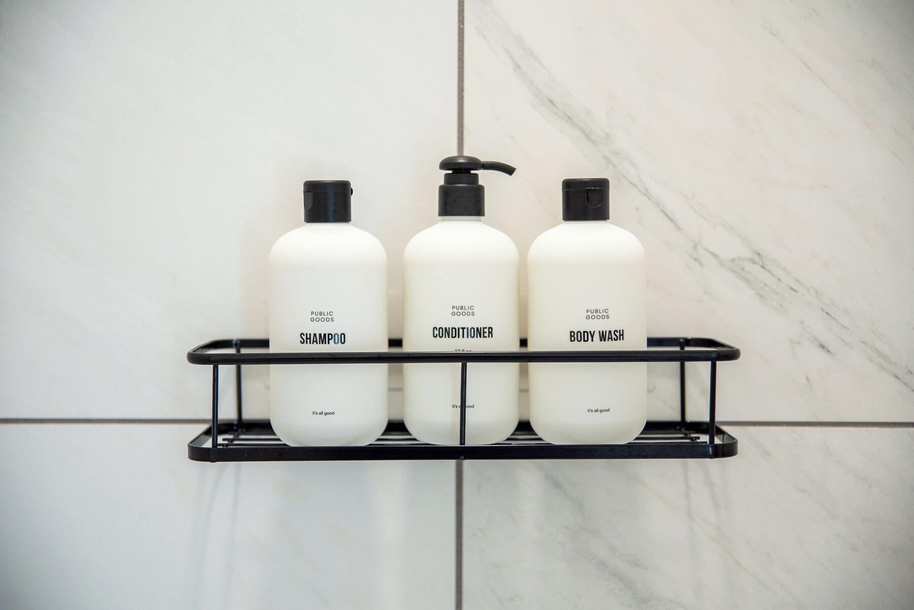 A bathroom shelf with three bottles of toiletries: shampoo, conditioner, and body wash.