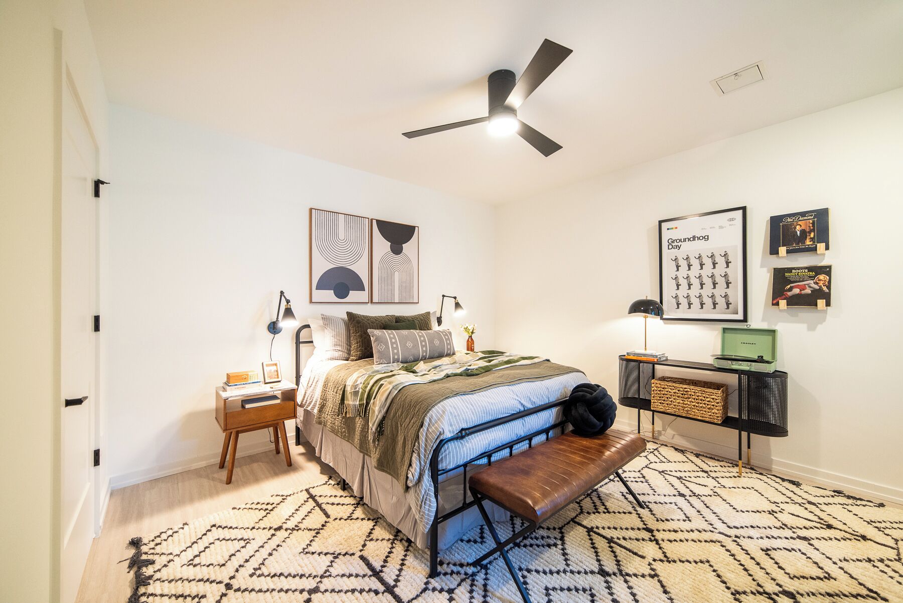 Une chambre à coucher comprenant un lit, des tables de chevet, un banc, un ventilateur de plafond et des œuvres d’art murales.