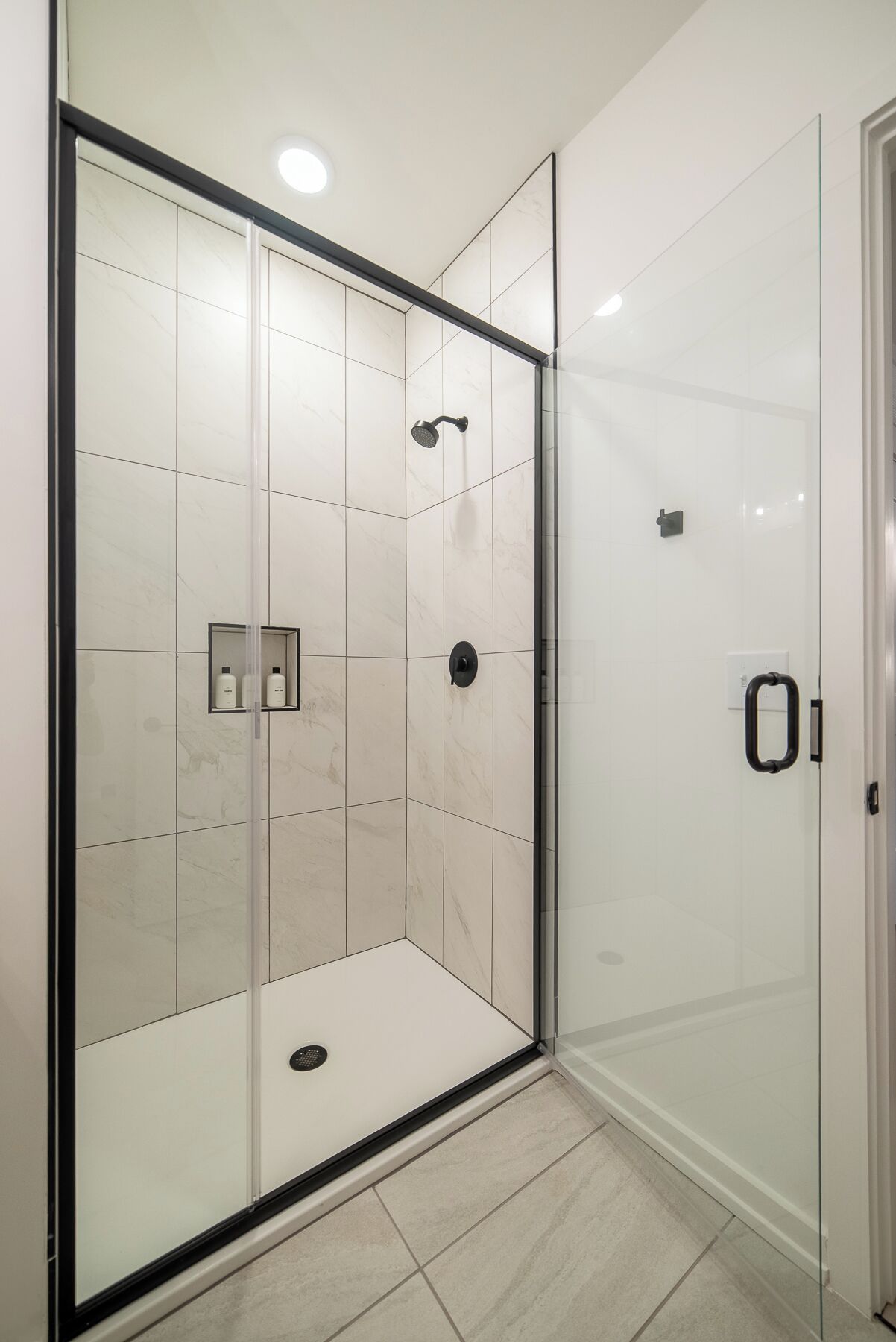 Une salle de bain moderne avec une douche à parois de verre, des murs recouverts de carreaux blancs et une porte dotée d'une poignée.