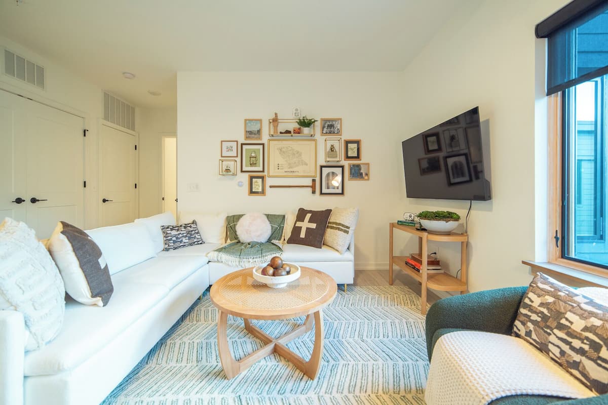 A living room with a white sofa, a round wooden coffee table, and a TV mounted on the wall.