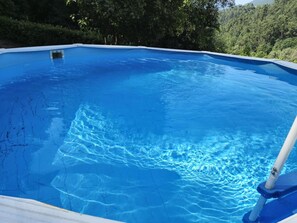 A clear blue swimming pool with a view of a forested hillside.