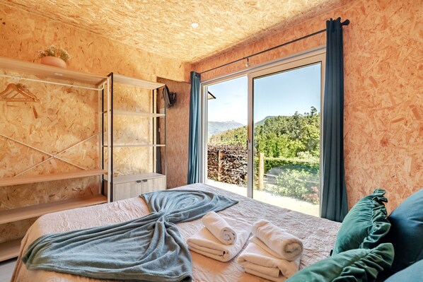 Ein Schlafzimmer mit Bett, Handtüchern, einer Holzbalkendecke, einem Fenster mit Blick und einem Regal mit Pflanze.