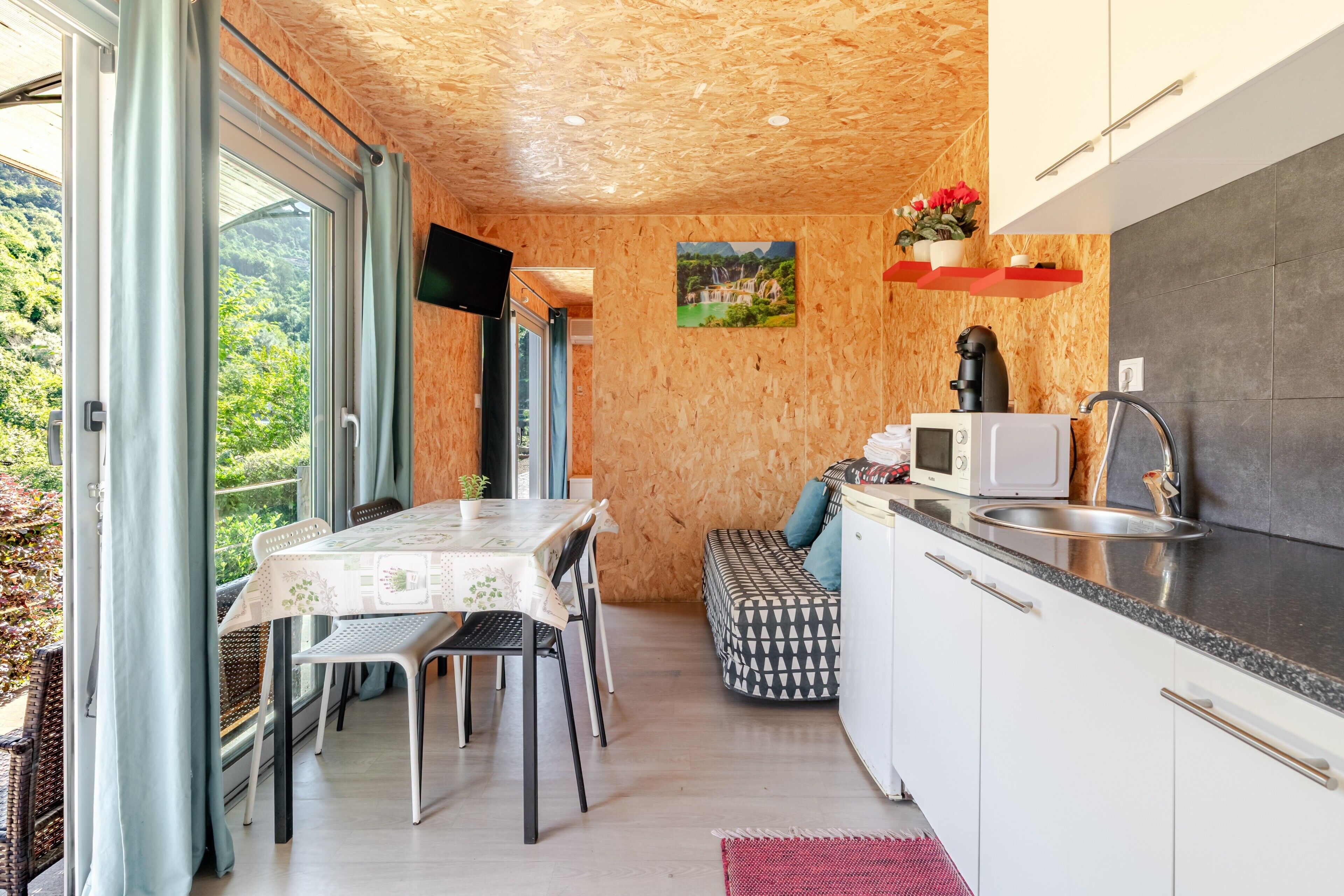 Eine moderne Küche mit Holzbalkendecke, einem Essbereich mit Tisch und Stühlen sowie Blick ins Grüne.