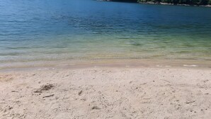 Una playa con agua cristalina, orilla arenosa y colinas boscosas al fondo.