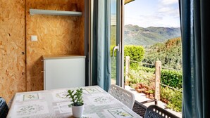 Una habitación con una mesa, sillas, una planta en maceta, un ventanal con vistas a un paisaje montañoso y una pared de madera.