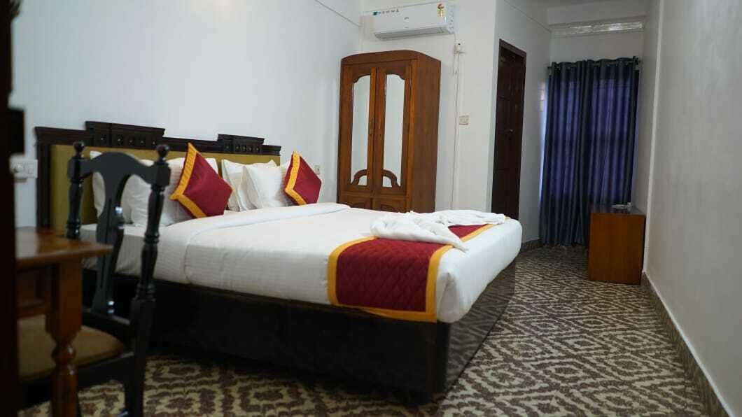 A hotel room with a bed, a wooden wardrobe, a desk, and a patterned carpet.