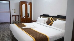 Hotellihuone, jossa on suuri sänky, puinen vaatekaappi ja tuoli.