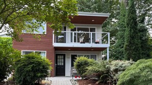 Een huis met twee verdiepingen, een voortuin, een pad van baksteen en diverse struiken en bomen.
