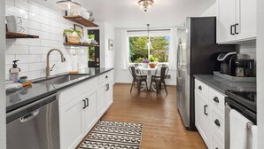 Een moderne keuken met witte kasten, roestvrijstalen apparatuur en een eetgedeelte met een tafel en stoelen.