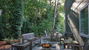 Een terras buiten met een vuurkuil, zitplaatsen en uitzicht op een bebost gebied.