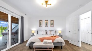 Ein modernes Schlafzimmer mit einem großen Bett, zwei Nachttischlampen, einer Bank und einer Schiebetür zu einem Außenbereich.
