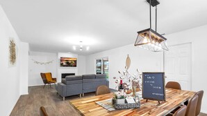 Ein modernes Wohnzimmer mit einem grauen Sofa, einem Holzesstisch mit vier Stühlen und einer Hängeleuchte.