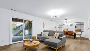 Ein modernes Wohnzimmer mit einem grauen Ecksofa, einem Holztisch und einem Essbereich mit Holztisch und Stühlen.