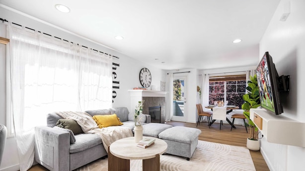 A modern living room with a grey sofa, a round coffee table, and a dining area with a white table and chairs. - Modern 2BR Gem , Near UW & Lake Trails & Garage (Seattle)