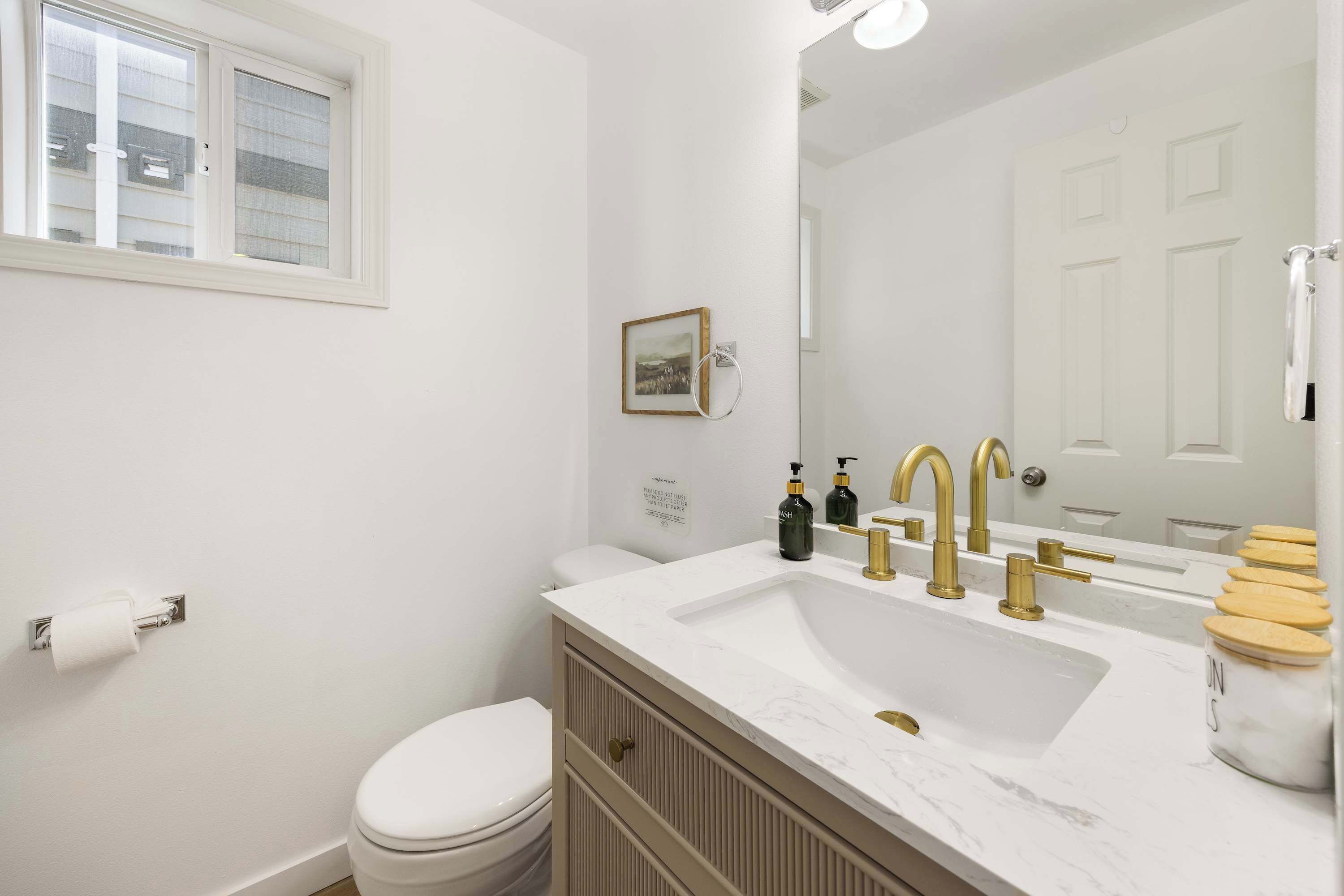 Une salle de bain avec des toilettes blanches, un lavabo doté de robinetterie dorée et un miroir au-dessus du lavabo.