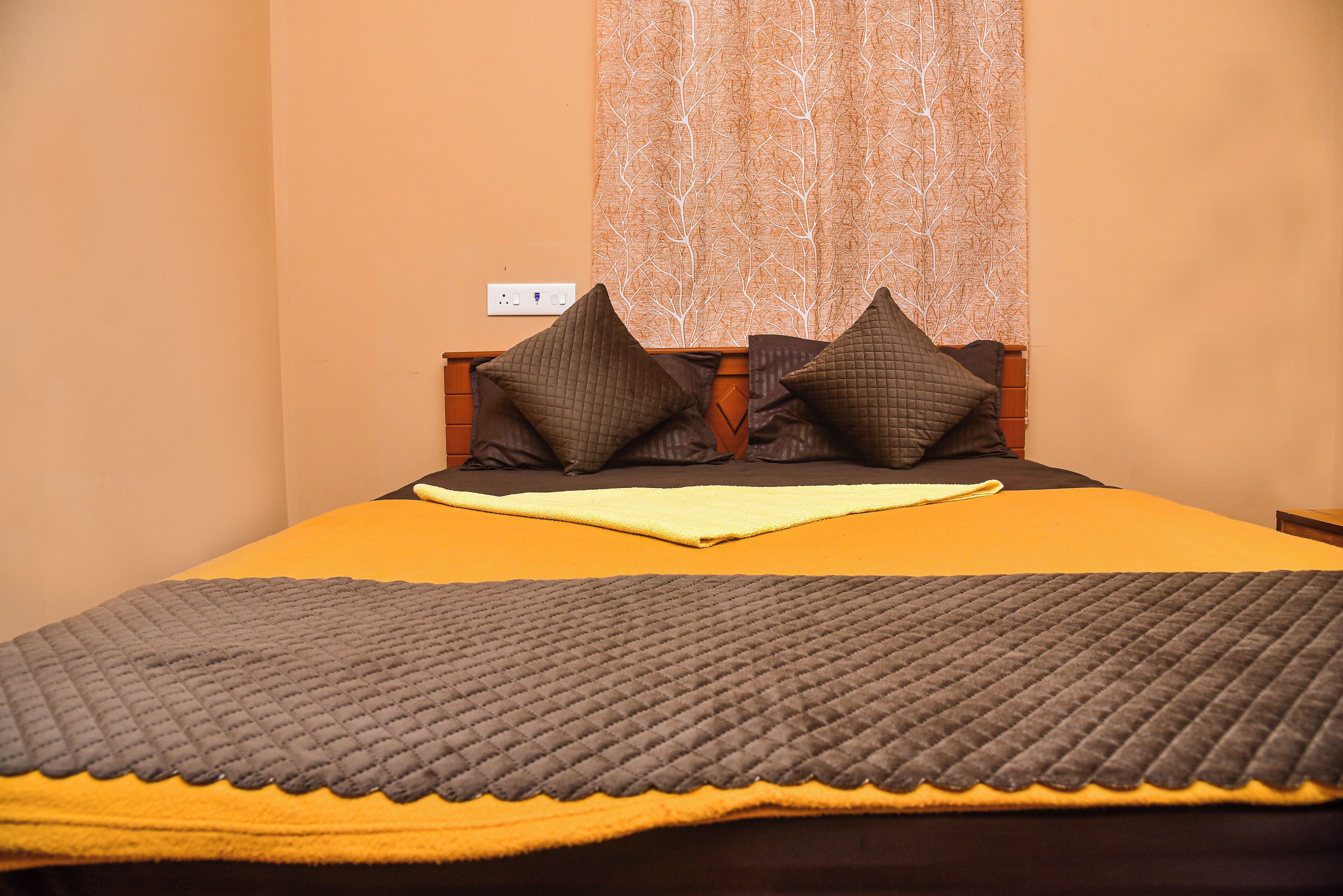 A bed with a yellow bedspread, two brown pillows, and a gray quilted blanket.