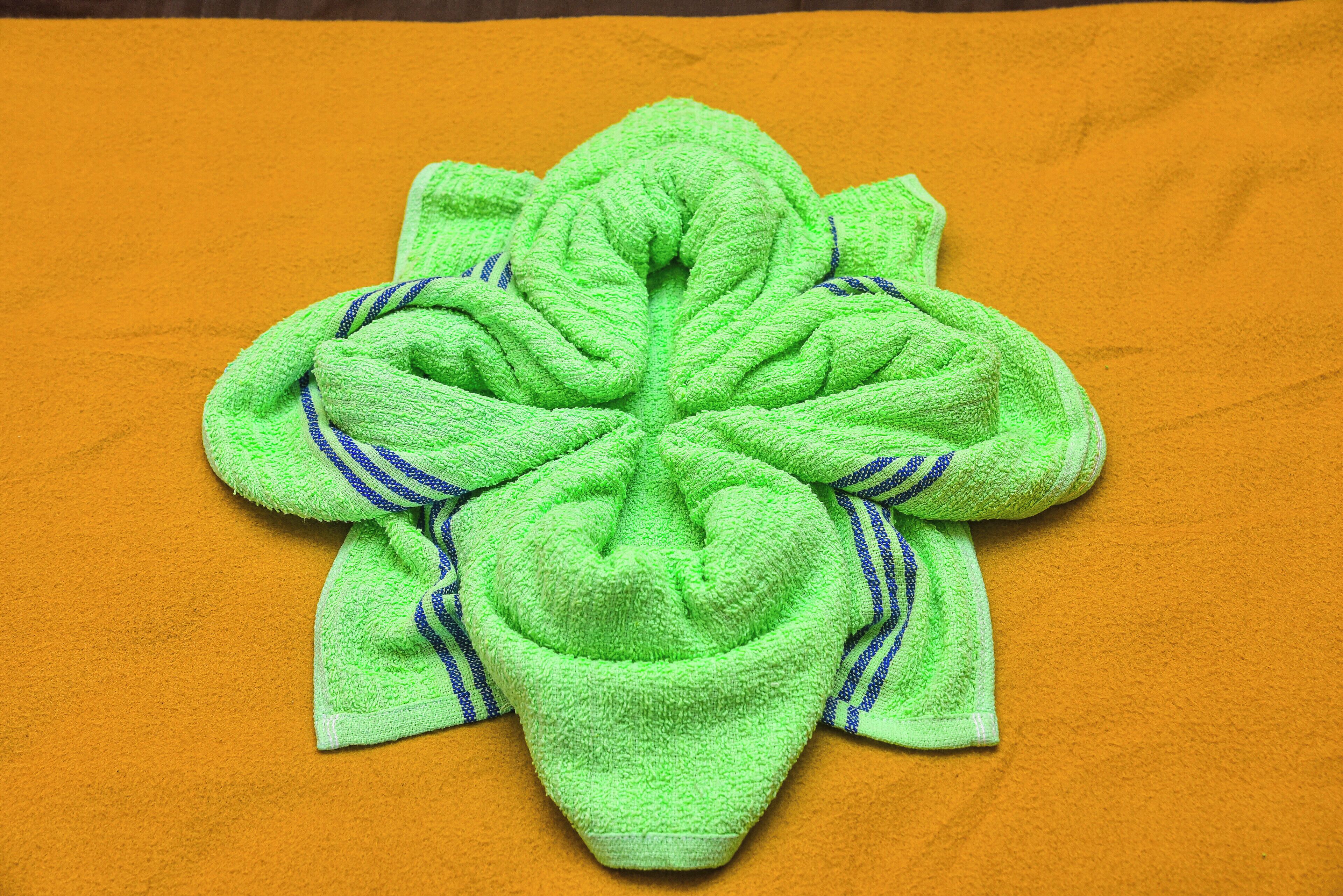 A green towel with blue stripes folded into a flower shape on an orange surface.
