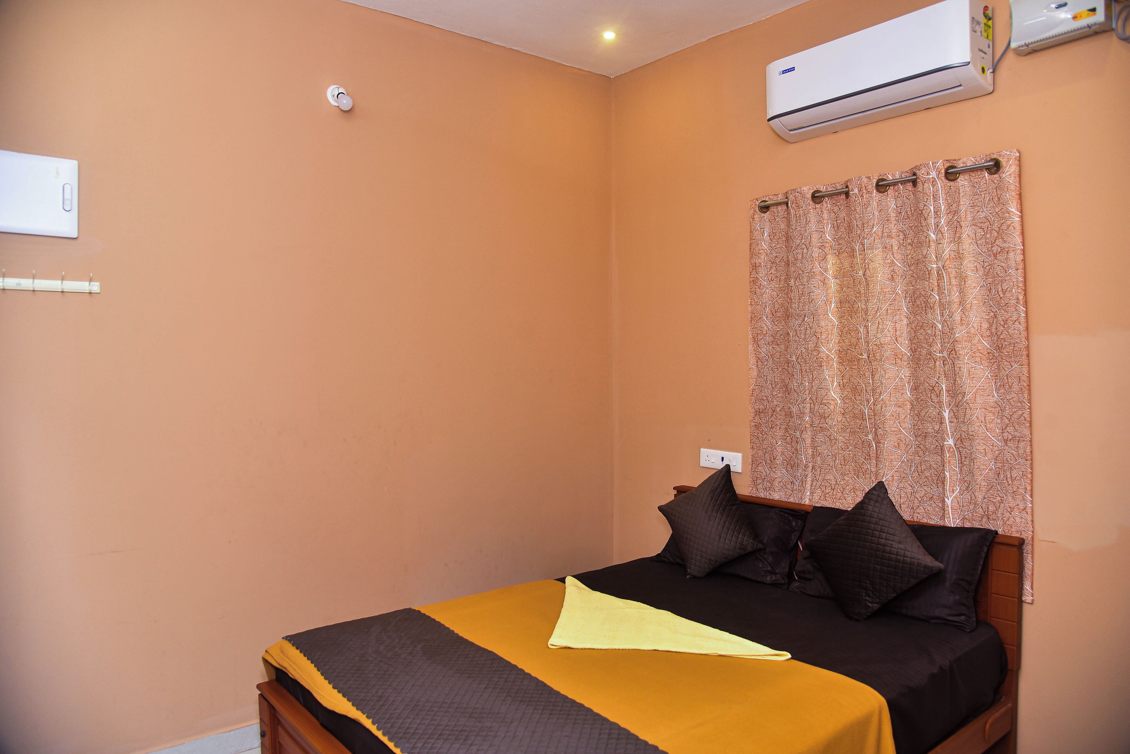 A bedroom with a bed, a curtain, an air conditioner, and a wall-mounted light fixture.