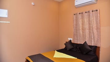 A bedroom with a bed, a curtain, an air conditioner, and a wall-mounted light fixture.