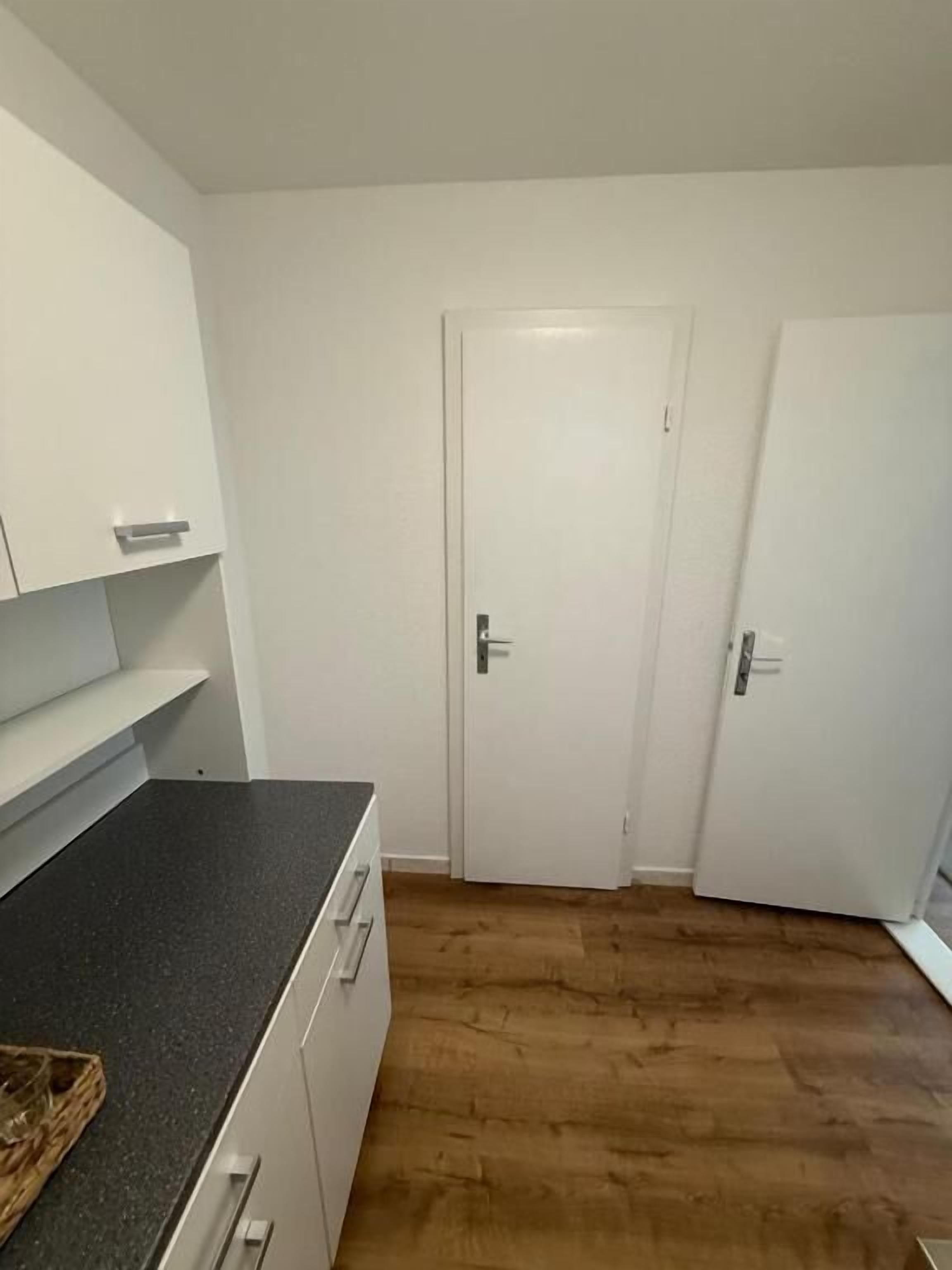 A kitchen with white cabinets, a black countertop, and a wooden floor.