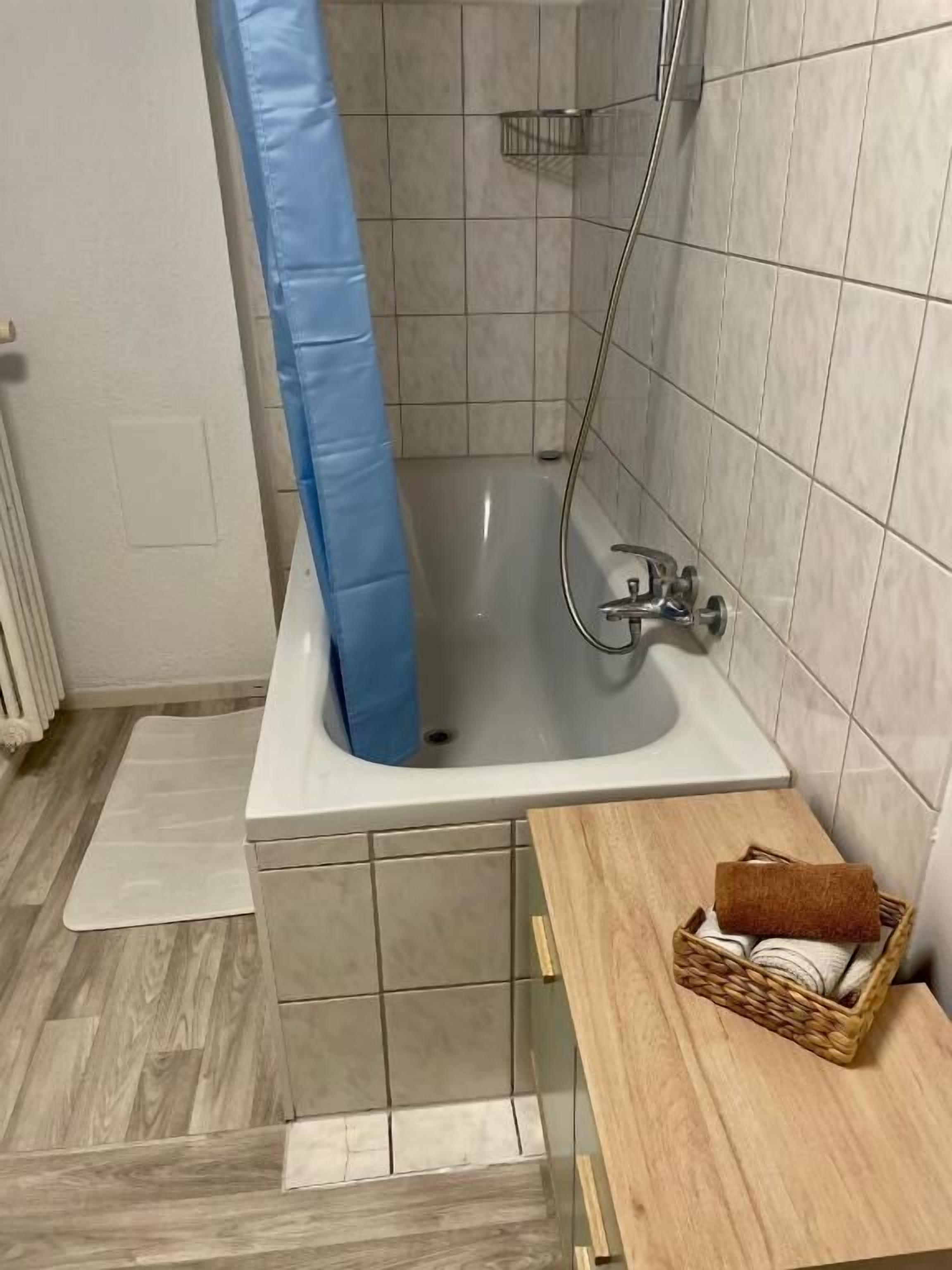 Ein Badezimmer mit einer Badewanne, einer Dusche und einer Holzbank mit einem Korb.
