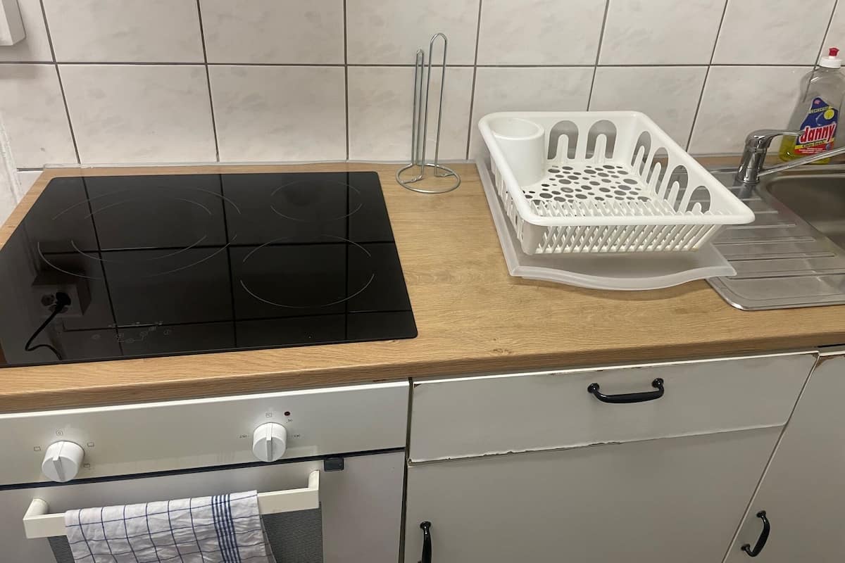 Une cuisine avec une plaque de cuisson à induction noire, un égouttoir en plastique blanc et une bouteille de liquide vaisselle posée sur le comptoir.