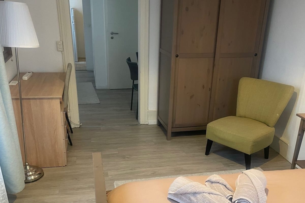 Une chambre d’hôtel avec un lit, une chaise, une armoire et un bureau avec une lampe.