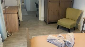 A hotel room with a bed, a chair, a wardrobe, and a desk with a lamp.