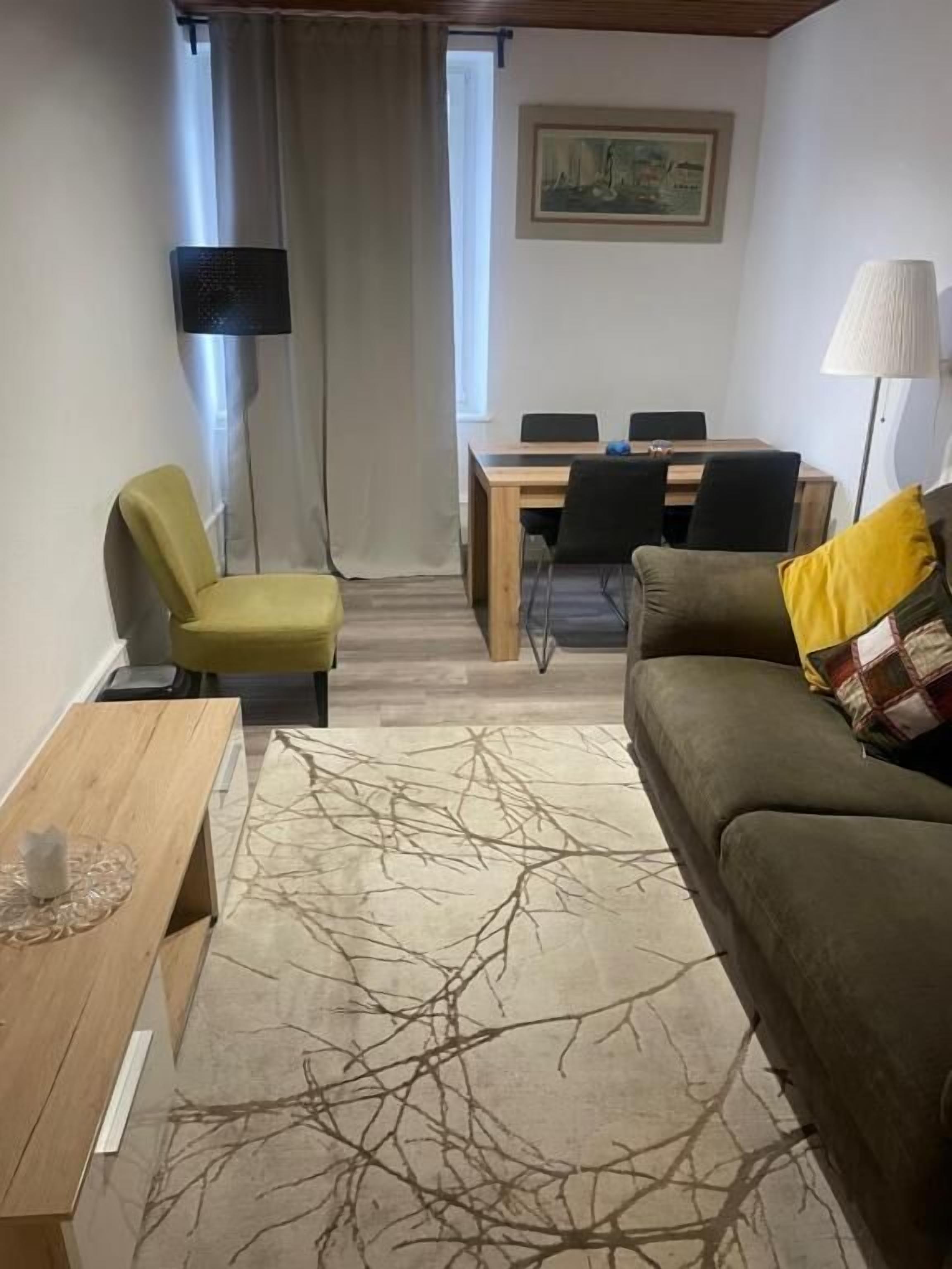 A compact living room with a sofa, a small table, a dining table with chairs, a lamp, and a painting on the wall.