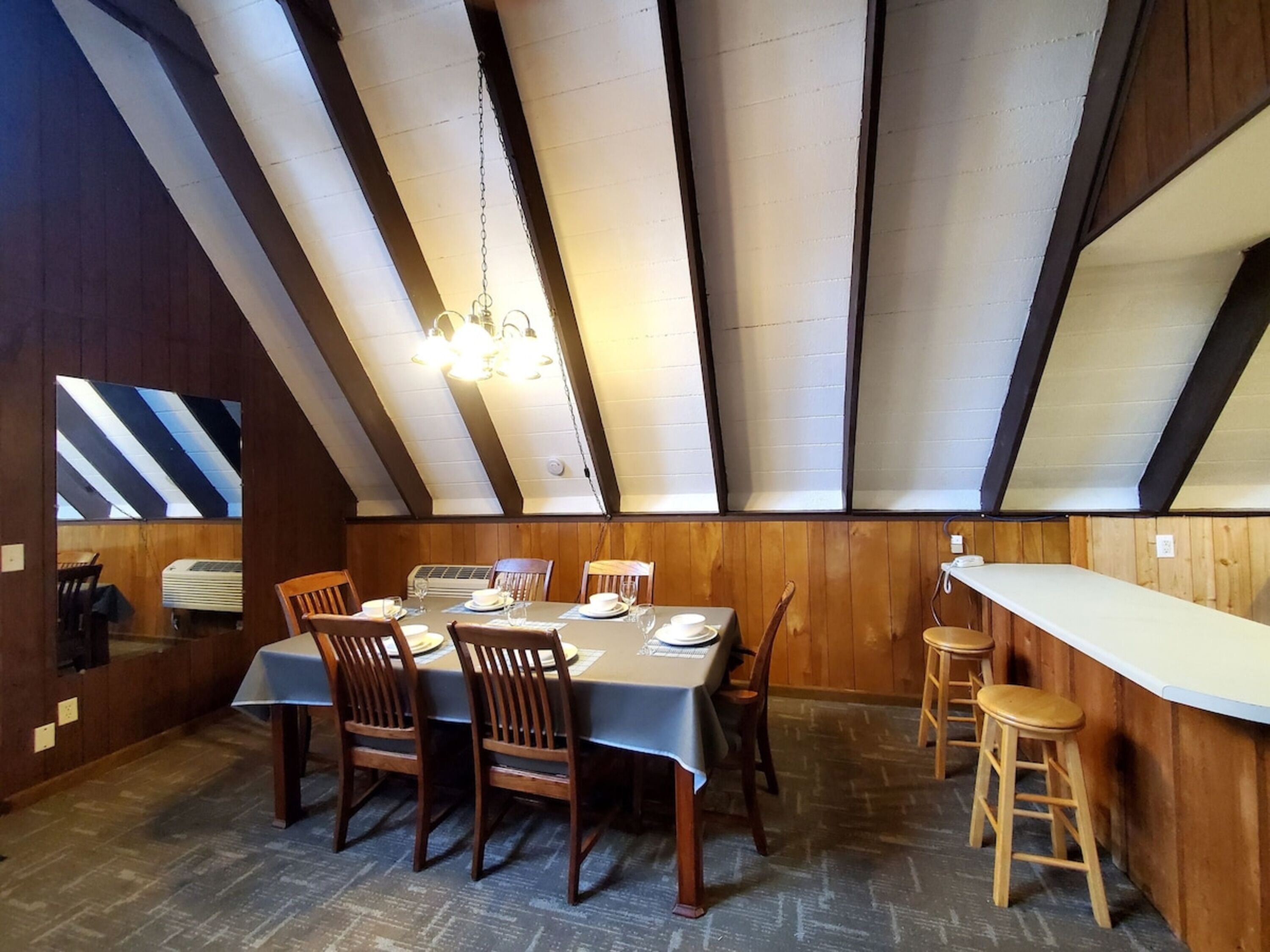 A dining area with a high ceiling, wooden panel walls, and a table set for six.