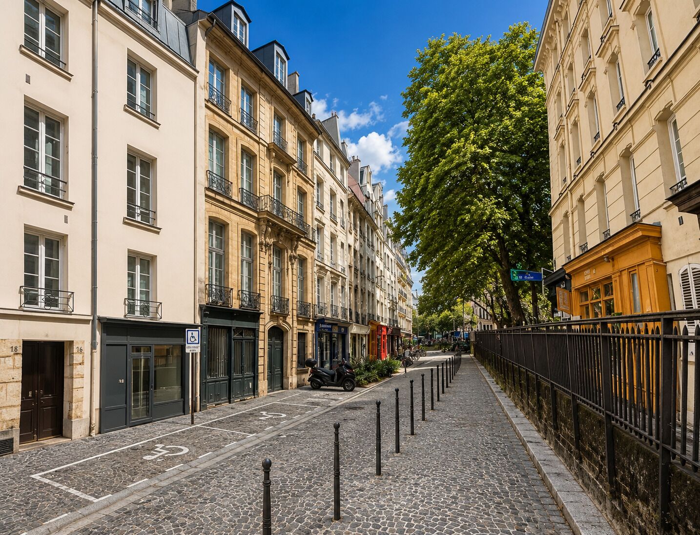 A cobblestone street lined with historic buildings, a scooter parked on the sidewalk, and a tree providing shade.