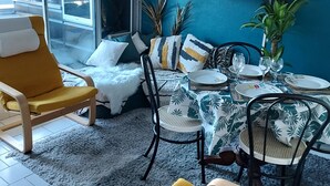 A modern living room with a yellow armchair, a dining table set with plates and glasses, and a blue accent wall. - Nice Apt with pool near the sea (Le Grau-du-Roi)