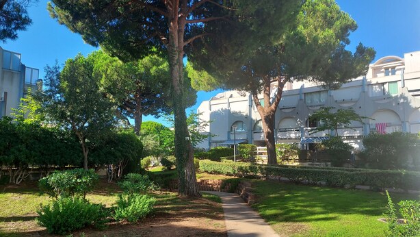 A courtyard with a pathway, trees, and a building with balconies and windows. - Nice Apt with pool near the sea (Le Grau-du-Roi)