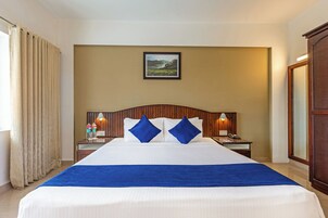 A hotel room with a large bed, two nightstands, a wooden headboard, a framed picture on the wall, and a window with curtains.