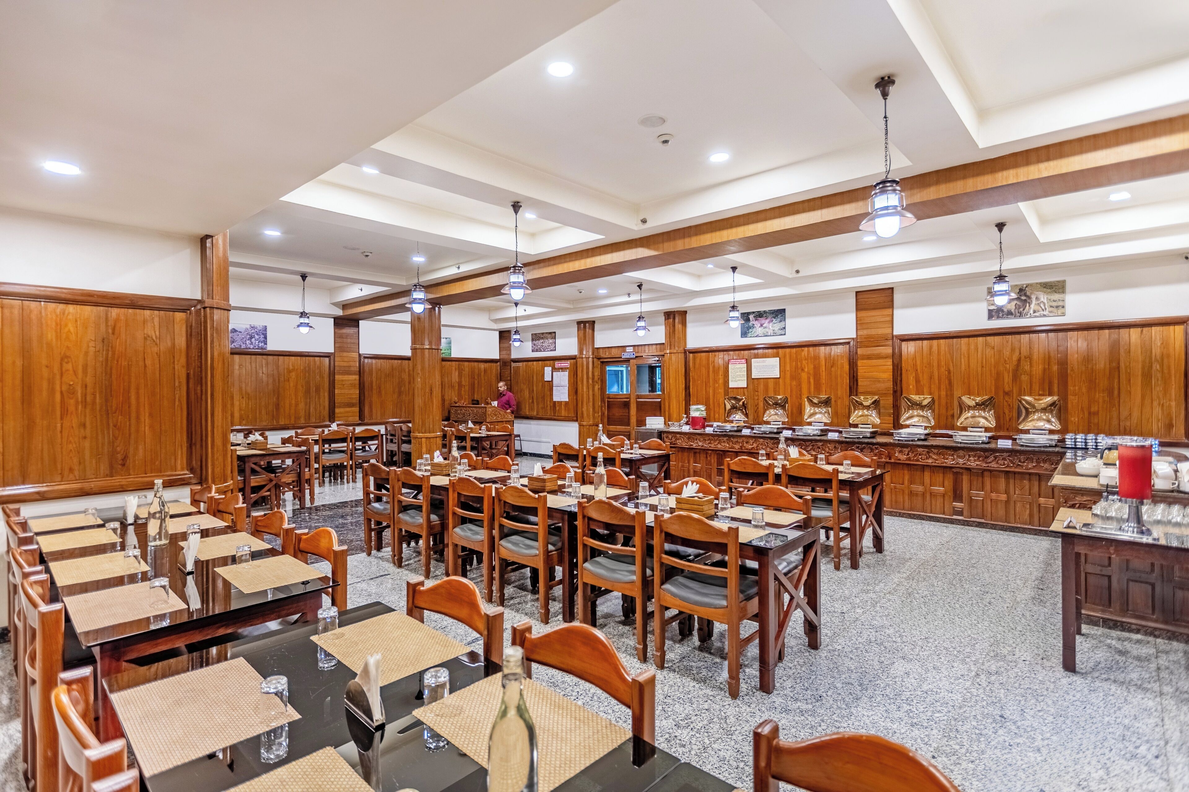 Un amplio comedor con múltiples mesas y sillas, paneles de madera y una zona de bar central.