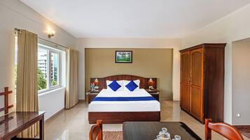 Una habitación de hotel con una cama grande, muebles de madera, una mesa de comedor con frascos y vistas a edificios a través de la ventana.