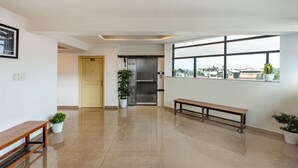 Un'ampia sala con una panchina, piante in vaso, una porta e una finestra con vista sulla città.