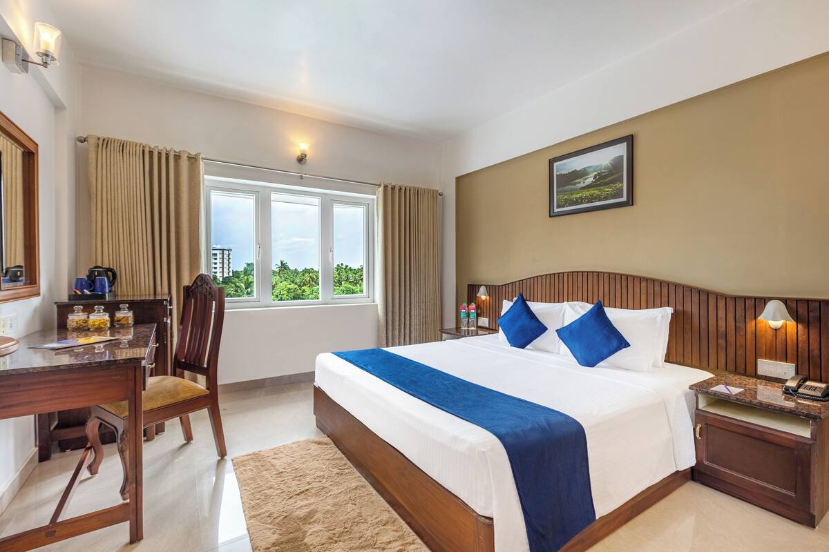 Una habitación de hotel con una cama grande, un escritorio con una silla, una ventana con cortinas y vistas al exterior con vegetación.