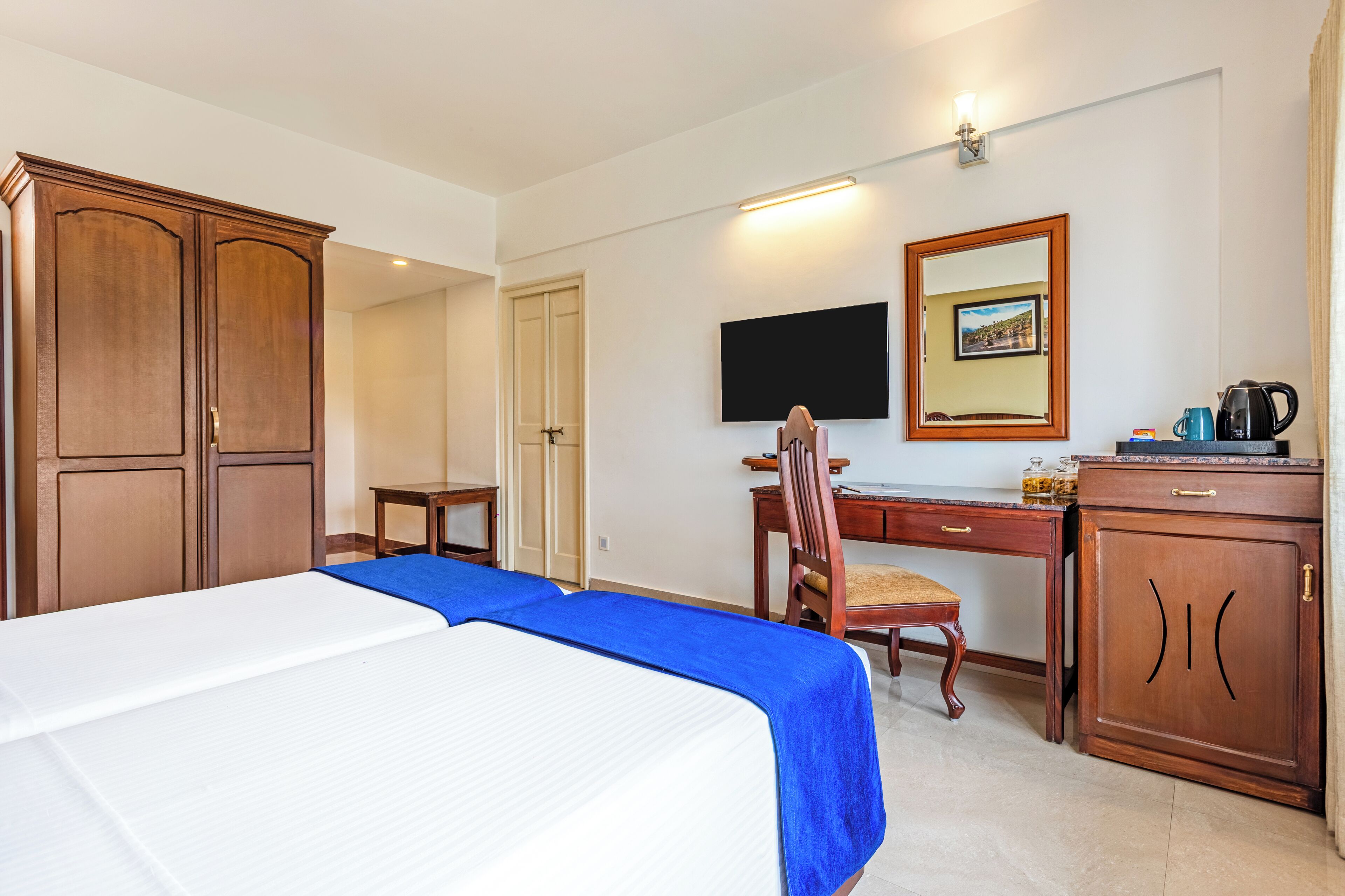 Habitación de hotel con cama, escritorio, silla, armario, televisor y cafetera.